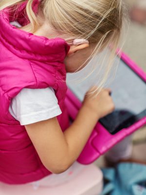 Young blonde deaf girl wearing a hearing aid using a tablet device