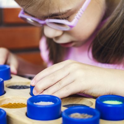 Child with poor vision is touching the wooden tactile rolls of different texture and colour as a part of educational therapy. AdobeRGB profile.